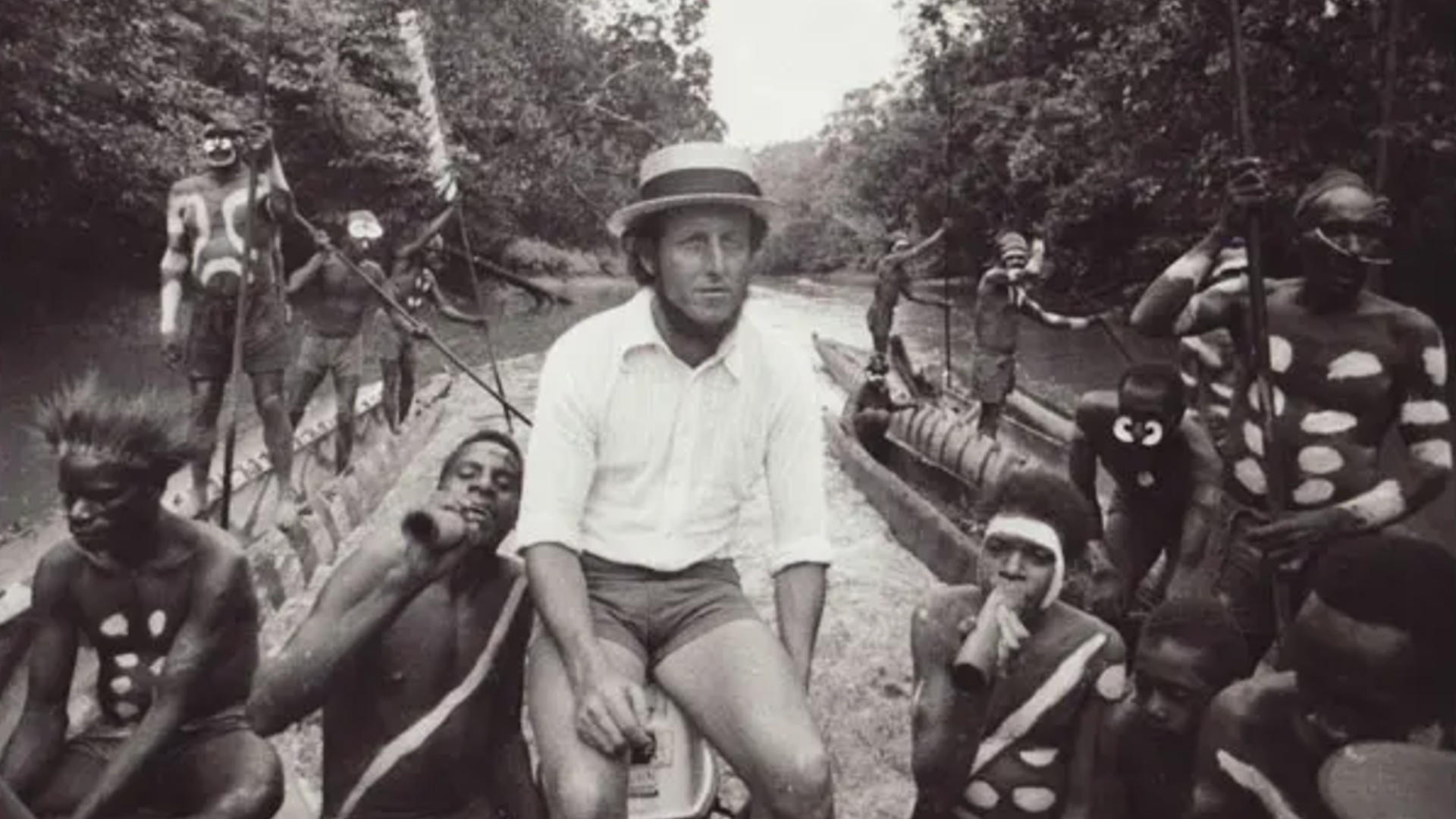 Researcher Lyall Watson sitting with some native peoples in a boat, surrounded by vegetation.